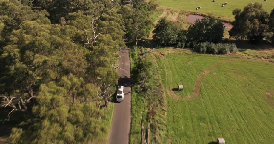 A white trailer driving on a paved road in a rural area with large green pastures on the sides