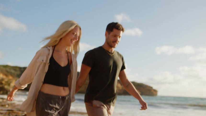 A couple walks hand in hand along a sandy beach next to the ocean