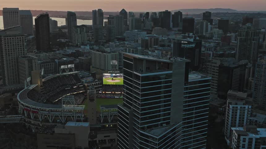 An aerial view of a large sports stadium in the middle of a metropolitan city with huge buildings