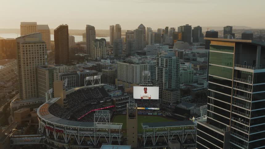 A baseball stadium sits amidst a bustling cityscape at sunset