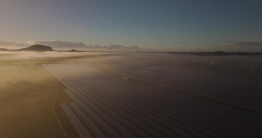 An aerial view of a solar panel farm and there is heavy fog hanging over the area
