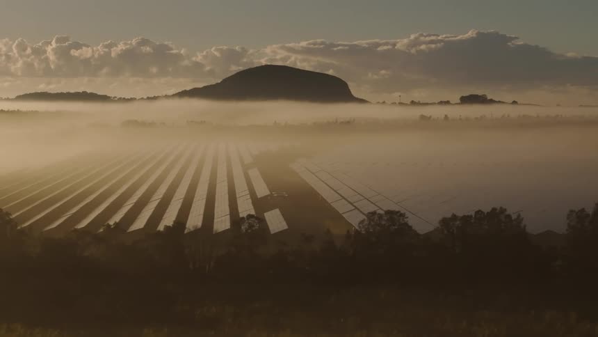 An aerial of dense fog in a valley with solar panels in it as the sun rises on the horizon lighting up the sky