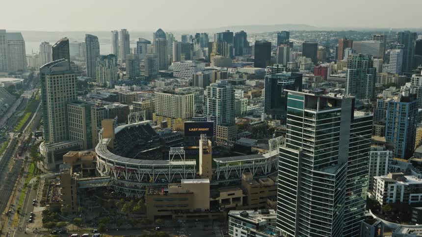 Video plays on a giant screen in a baseball stadium located in a dense downtown area