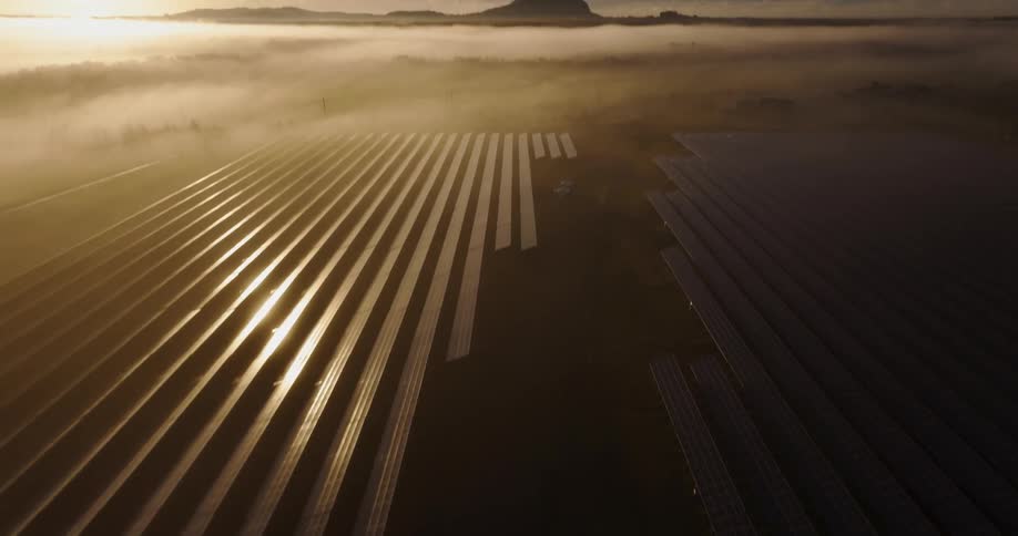 Bright sun glares from the horizon onto a foggy field containing solar panels
