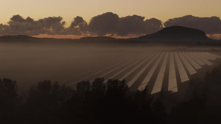 Solar panels fill a large plain between a forest and a mountain range