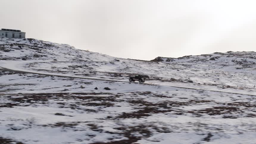 A jeep travels up a mountain road to a rural house on a winter day
