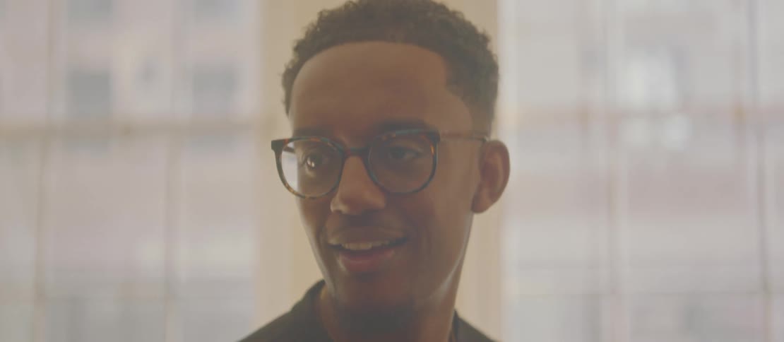 A young black man smiles while playing the piano in a room