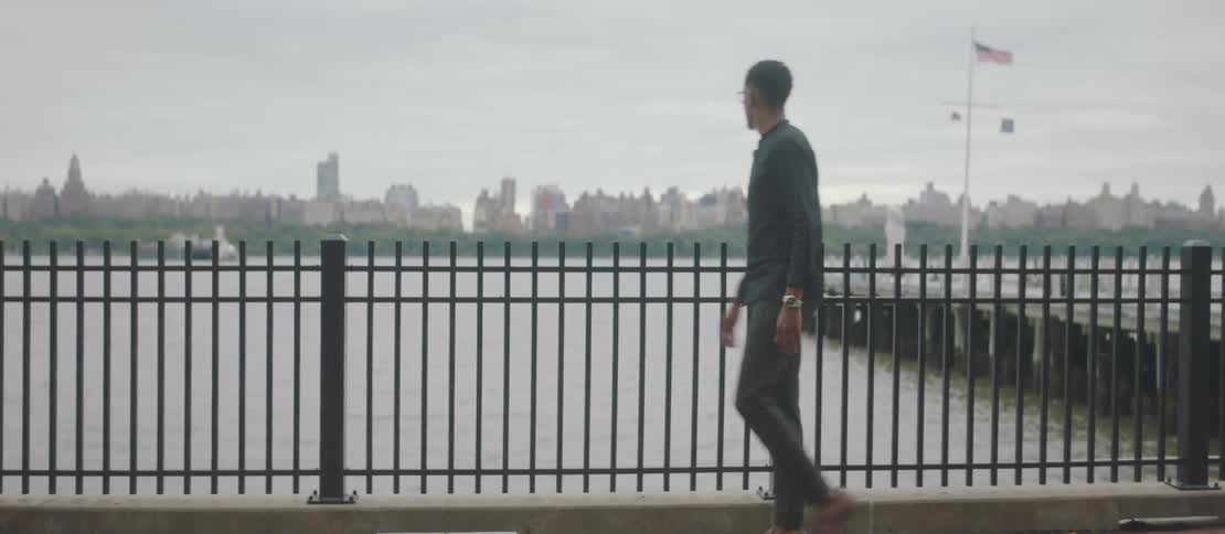 A man walks along a pier in front of a city skyline