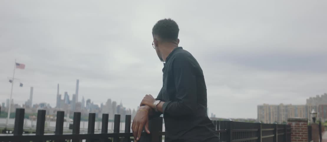 A man with his back to the railing is leaning and he is looking down and then forward