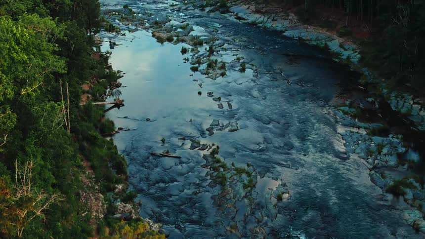 A river flows over rocks and rapids in a deep forest