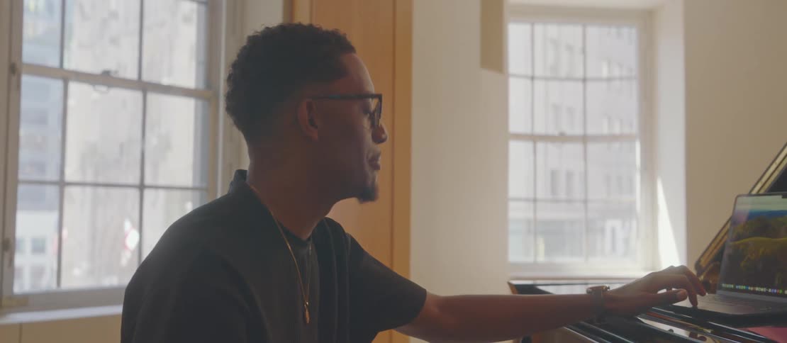 A joyful musician chats and laughs while using a laptop on a grand piano