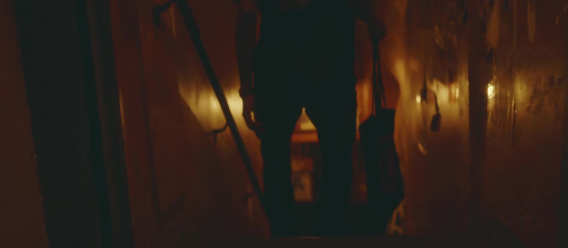 A man with his back turned walking towards a small tunnel with a ladder going down