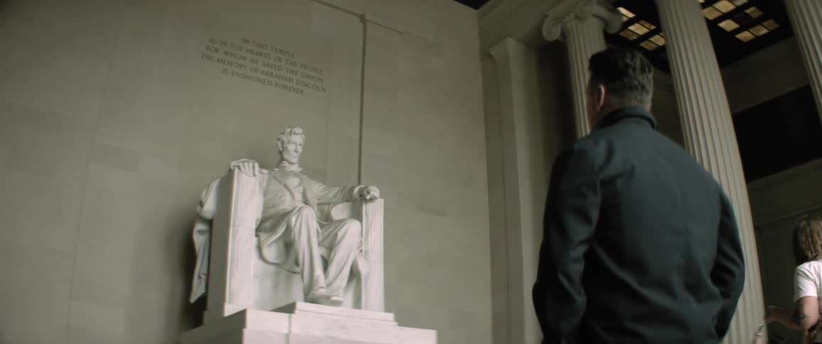 A man looks at a statue of lincoln at the lincoln memorial as visitors pass by