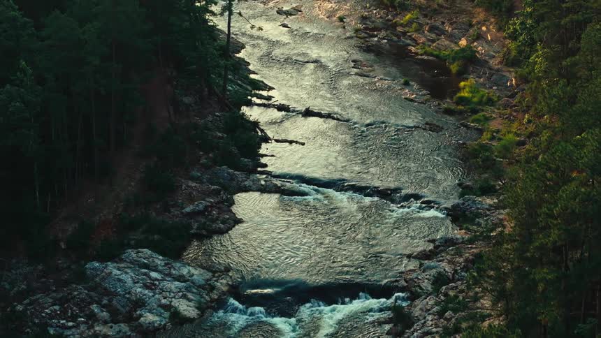 A shallow river flows over numerous rapids as it runs through a forest