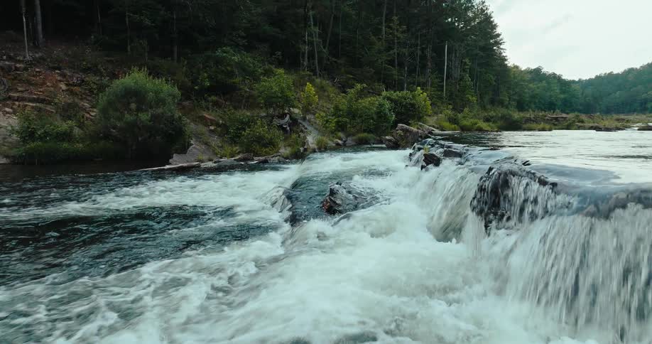 A river with a small waterfall with some rocks and a forest on the shore