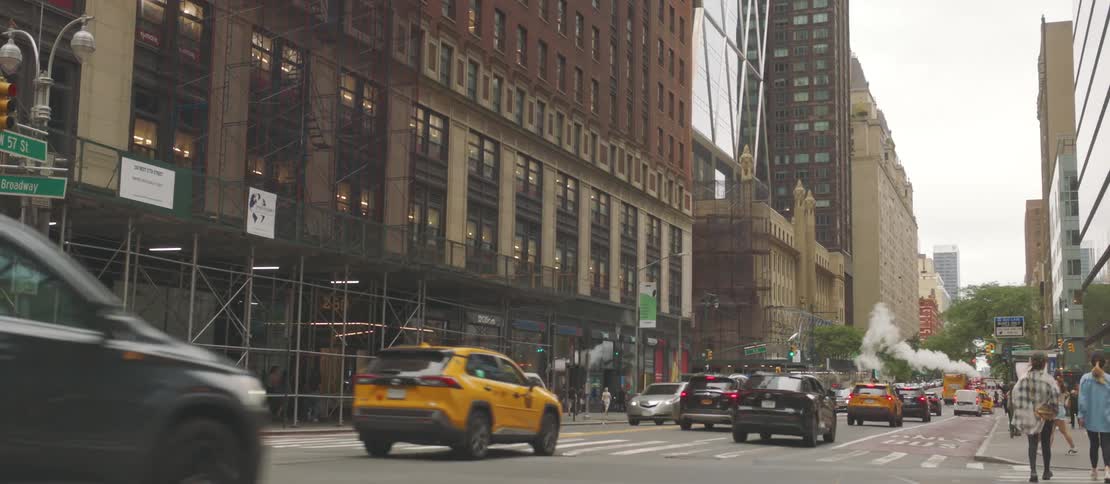Pedestrians and vehicular traffic pass the construction zone at the base of a downtown skyscraper