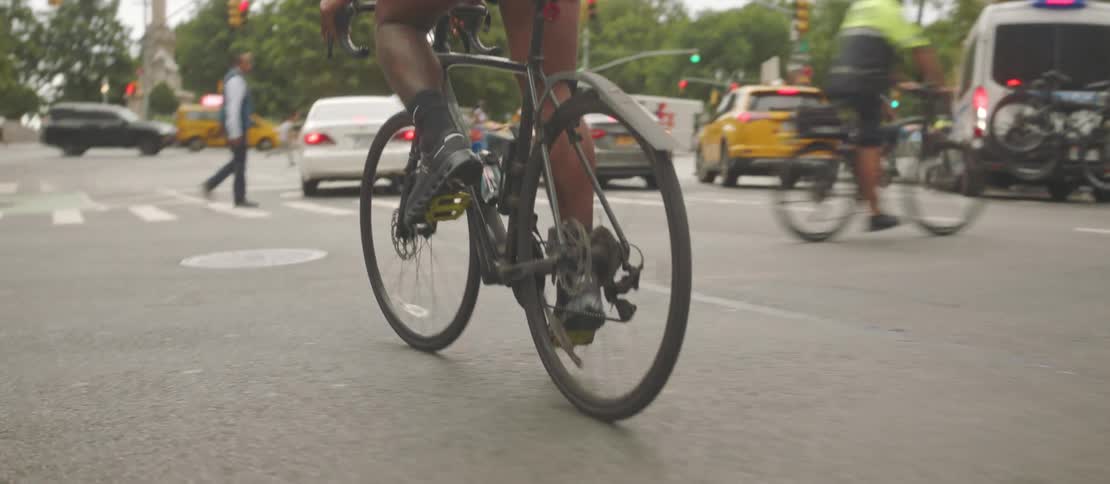 A person riding a bicycle on an asphalt street next to several cars stopped at a traffic light