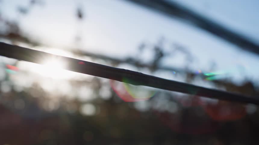 A closeup of a water droplet hanging from a pipe with the sun shining through the bokeh effect trees in the background