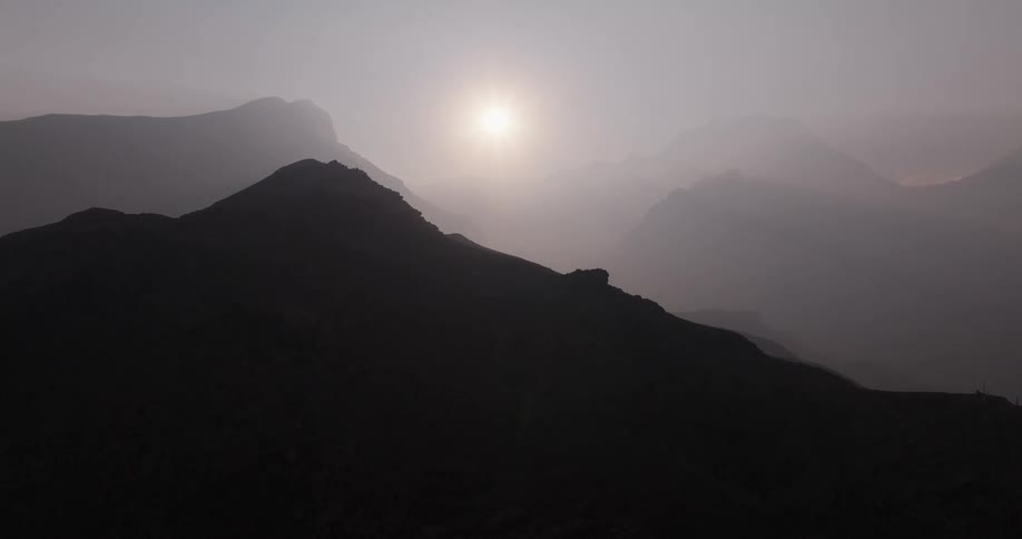 Sun casts mountains into silhouettes on a foggy day