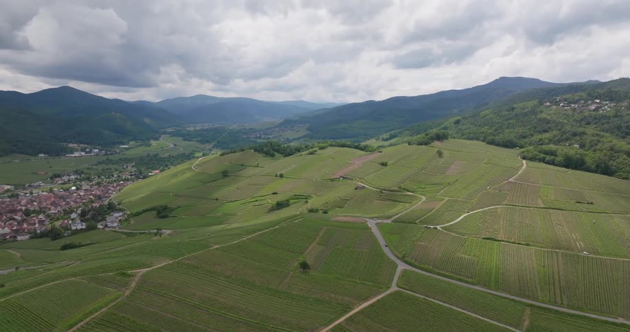 Aerial panorama of an agricultural field on hills surrounded by mountains and greenery and a city in the background