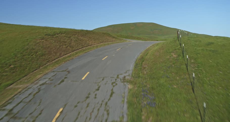 An aerial view of a rural area with several green fields of grass and an asphalt road that is eroded
