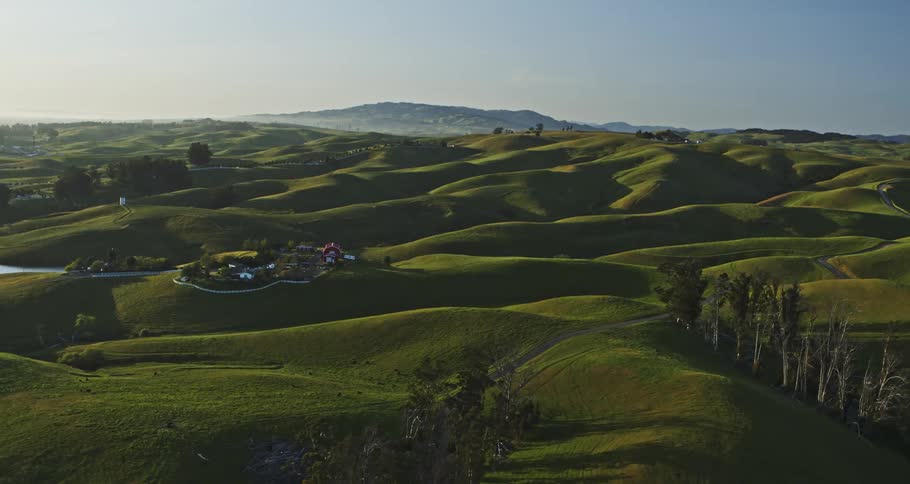 A rural farming community next to rolling hills and a mountain range on the horizon