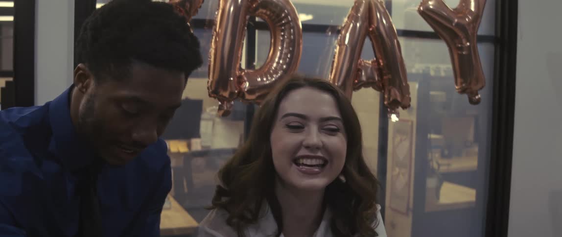 Two office employees sing happy birthday in an office