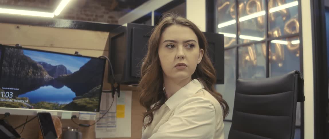 A woman with wavy hair and a white shirt is working on a computer in the office