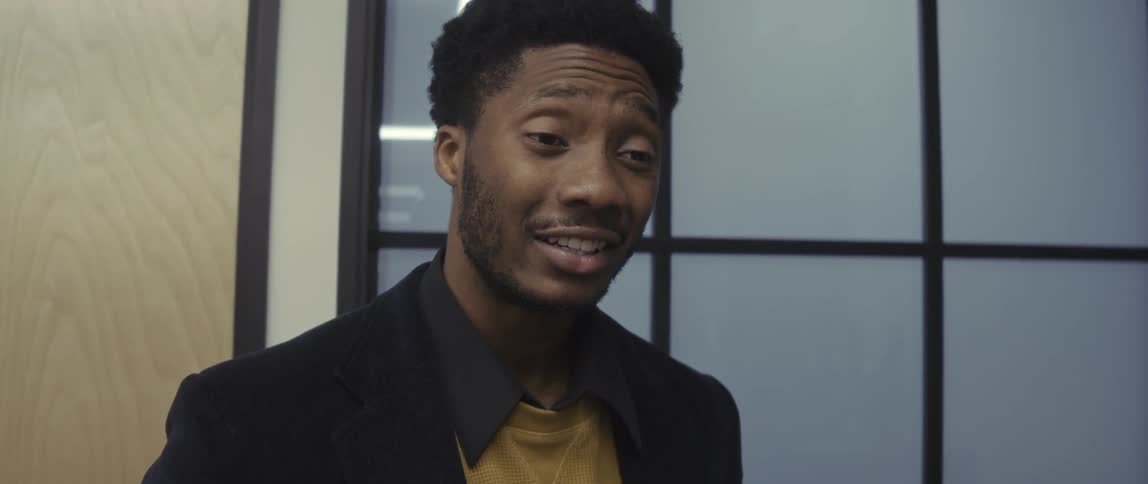 Two individuals in an office setting one a dark blazer over a mustard sweater engaged in conversation