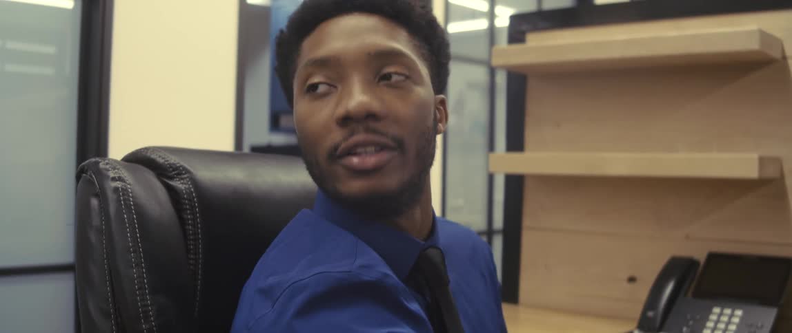 A male employee sits in a cubicle talking to someone nearby