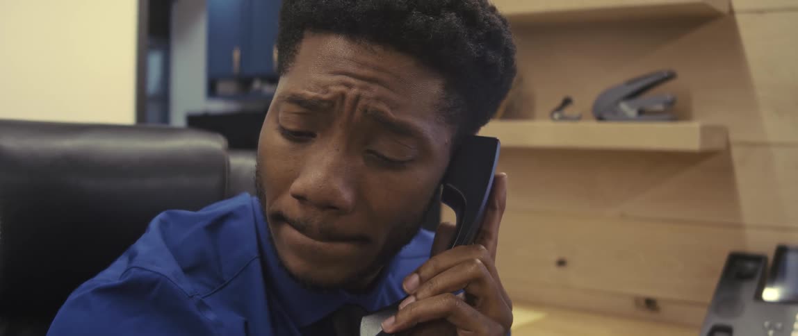 A male employee in an office sits in a chair and talks on an older style telephone