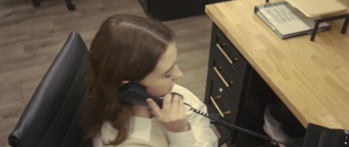 A woman typing on a keyboard in an office stops to answer a phone call