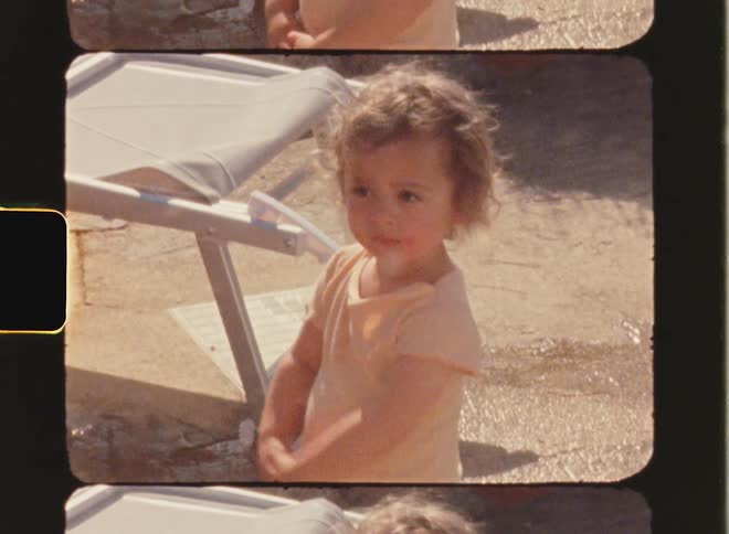 Super 8 film of a toddler who stands outdoors dressed in a vintage outfit captured on vintage film. The film has a light leak