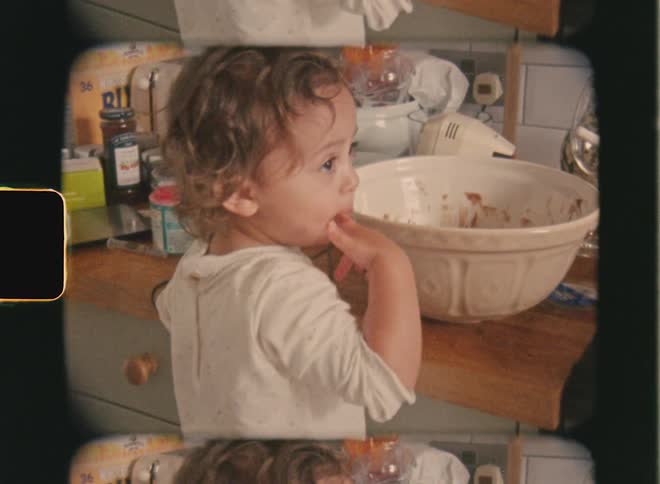 A young child stands in a kitchen eating chocolate from a mixing bowl captured on vintage super 8 film