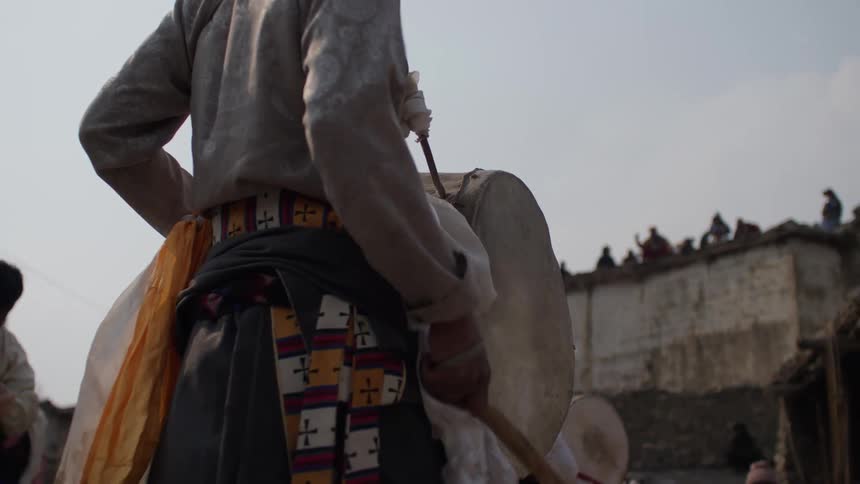 People in traditional attire play drums in the street