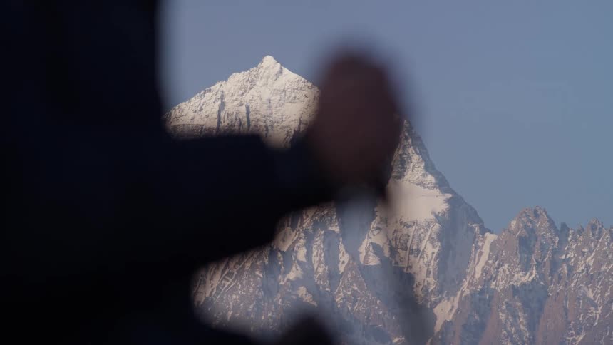 A hiker using trekking poles hikes through a field with snowcapped mountains in the background