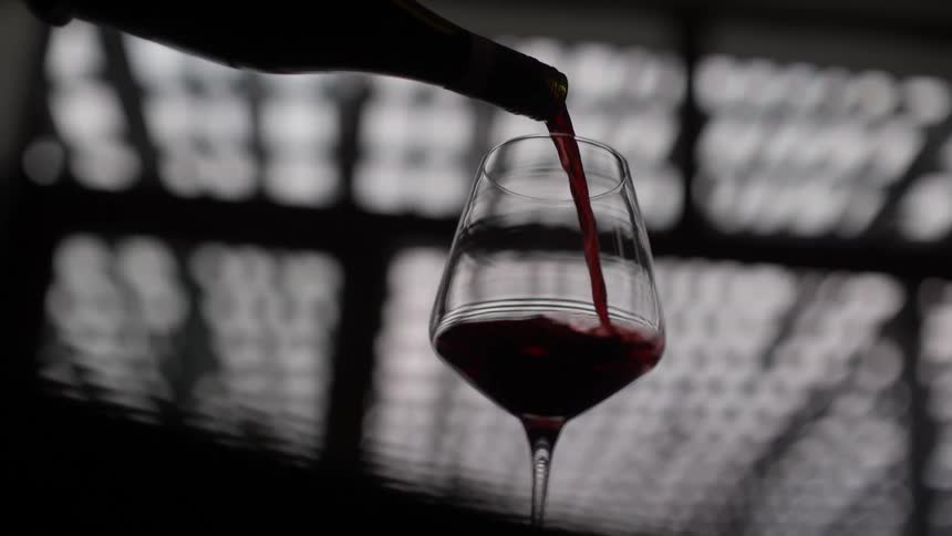 The silhouette of a wine bottle filling a clear glass