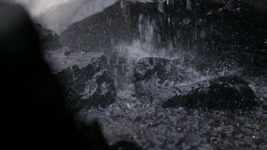 Water from a waterfall smashes into dark rocks
