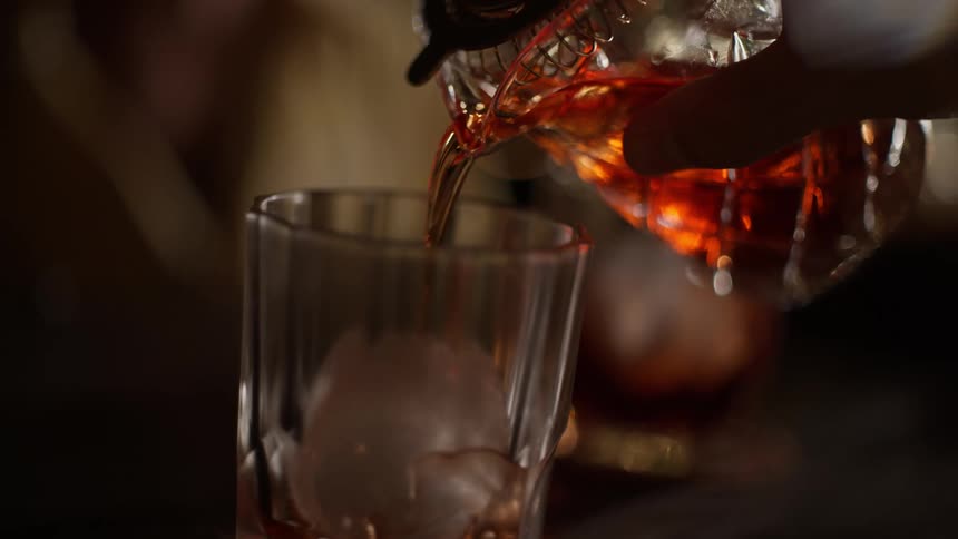 Alcoholic drink being poured into a whiskey glass with ice