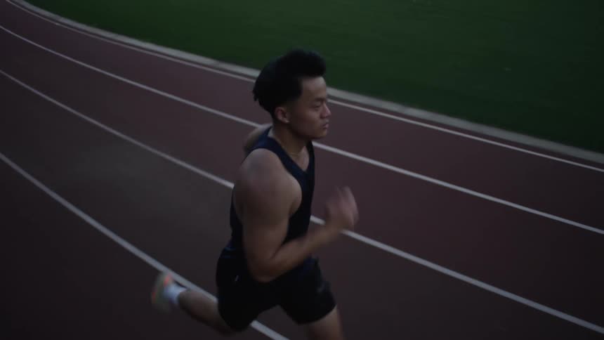 An asian man runs around a track during the summertime