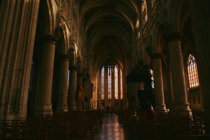 The interior of a dimly lit church with a stained glass window and rows of pews