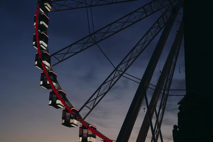 A large ferris wheel with lights spins slowly at dusk