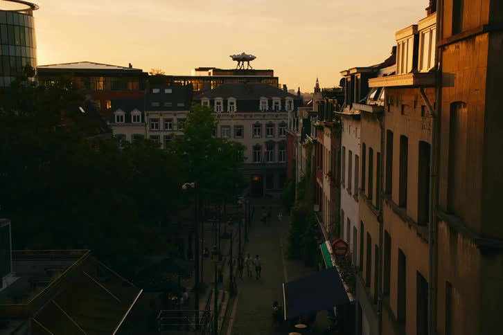 Pedestrians walk on the roadbetween a park and apartment buildings at sunset