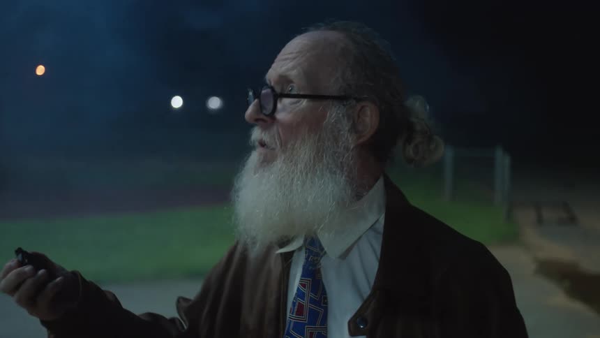 Elderly man with a long beard looking at a stopwatch while standing outdoors at night