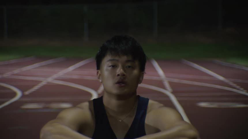 Young man sitting on a running track at night breathing shallowly
