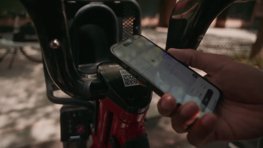 A hand uses a smart phone to scan a qr code and unlock a public use electric scooter
