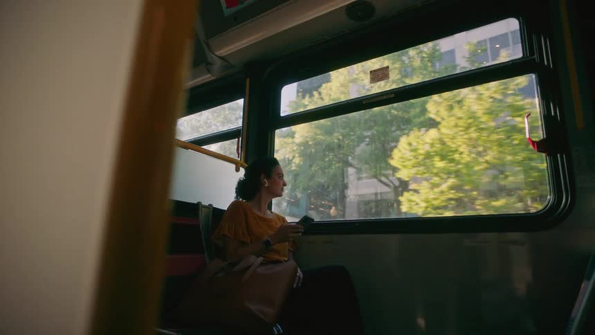 A woman listens to music on a smartphone as she rides a bus through a city