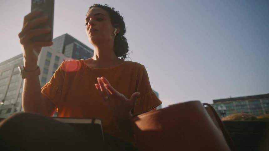 A woman sits and gestures while on a video call using her phone