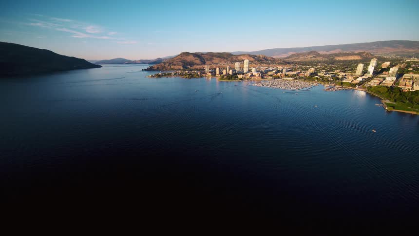Boats fill a marina on the waterfront of a city across the river from a mountain