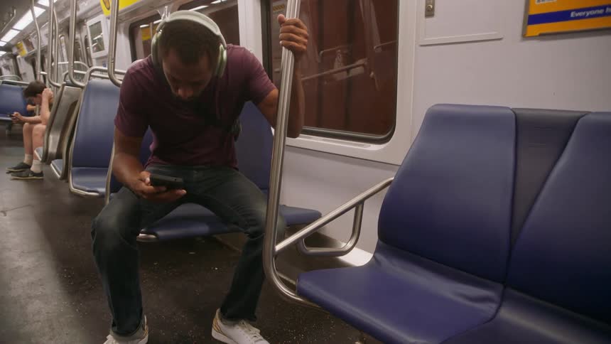Man boarding a train while wearing headphones and sitting on a bench